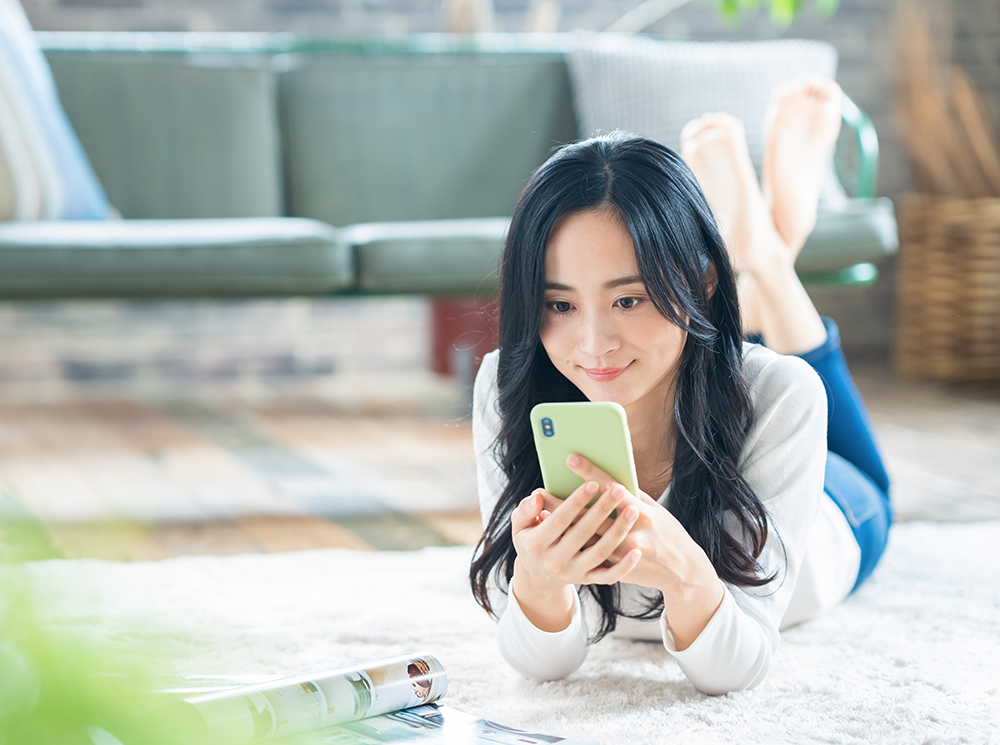 情報誌を見ながらスマホで検索する女性